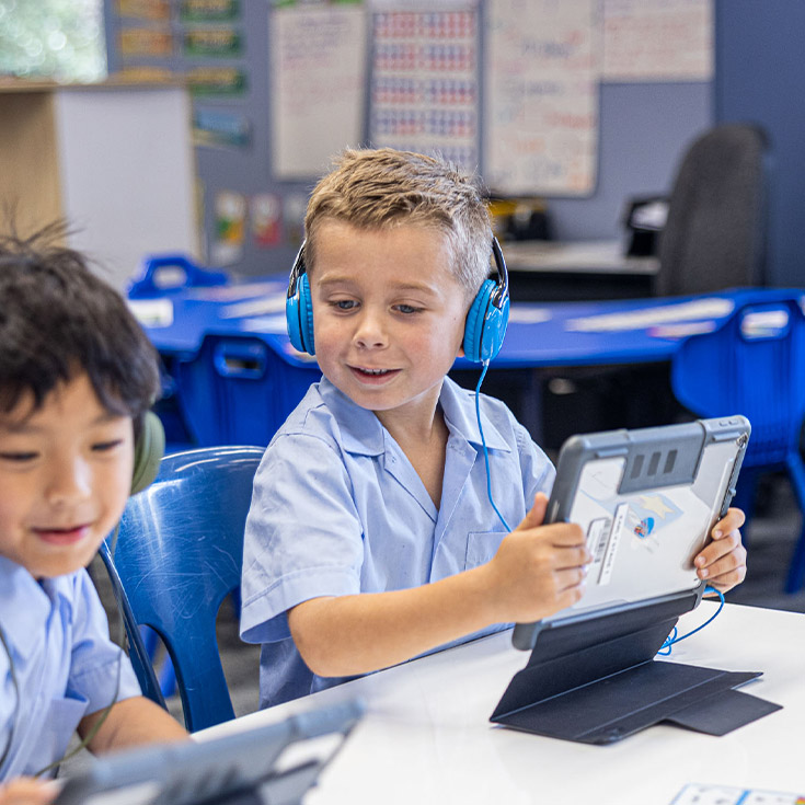 Student wearing headphones using his tablet in the classroom at St John's Primary School Riverstone