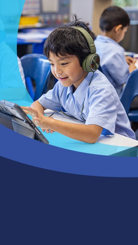 Student wearing headphones using his tablet in the classroom at St John's Primary School Riverstone